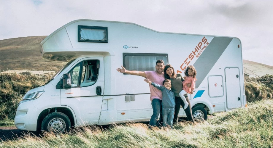 A family smiles together in front of their camper van, capturing a joyful moment during their outdoor adventure