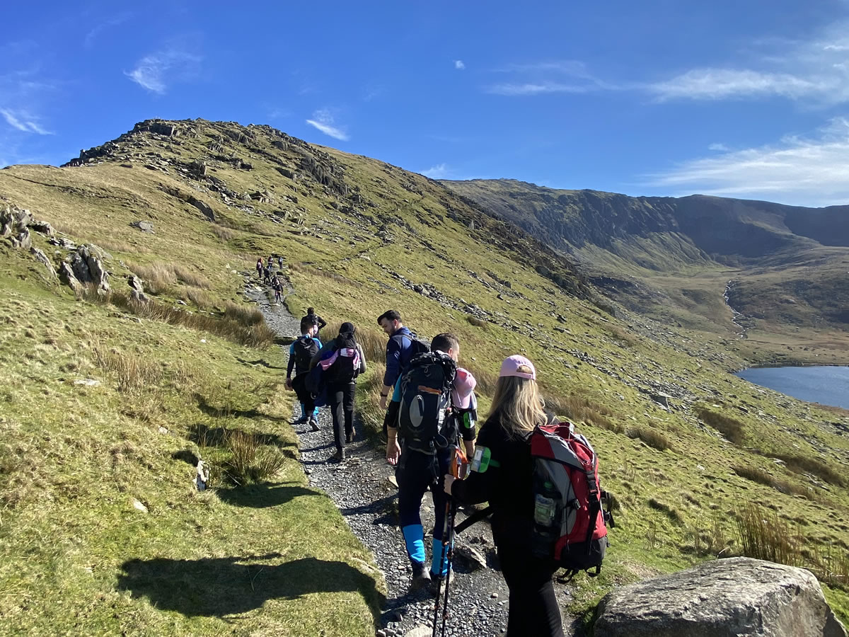 A diverse group of individuals hiking together on a scenic mountain trail, surrounded by lush greenery and rocky terrain